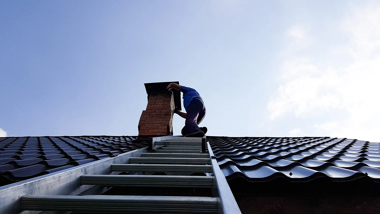 A man standing on top of a roof next to a ladder.